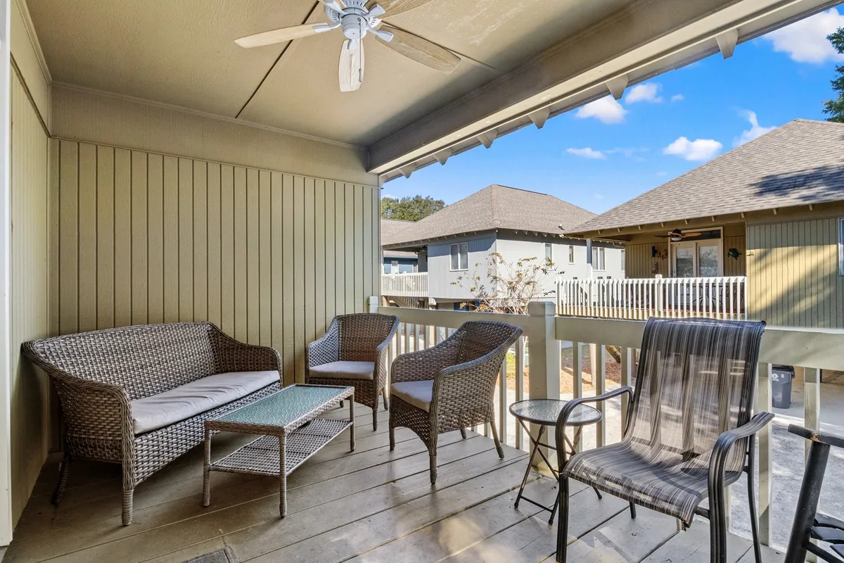 A cozy exterior porch featuring a wicker seating arrangement, glass-topped coffee table, and ceiling fan. The scene is inviting, perfect for enjoying a quiet morning coffee or relaxing with friends in the fresh air.