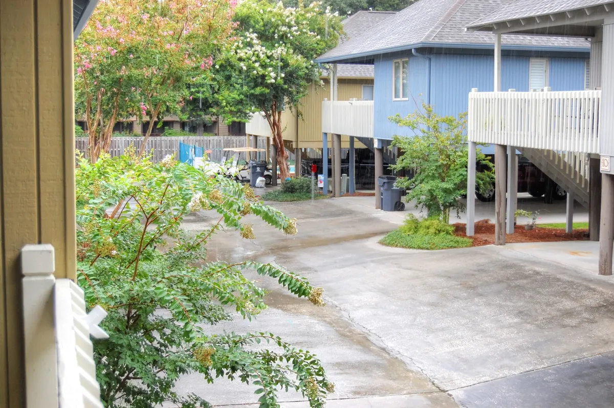 An exterior pathway bordered by green foliage leading past a blue building, offering views of a quiet parking area. The scene feels friendly and approachable, with easy access for vehicles and guests.