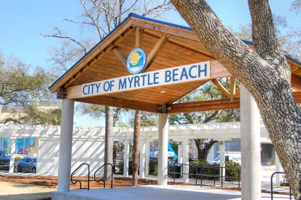 A community-focused exterior scene with signage and a wooden structure surrounded by trees, suggesting a venue for local gatherings, festivals, or outdoor concerts. The natural, shaded setting contrasts nicely with the more commercial images.
