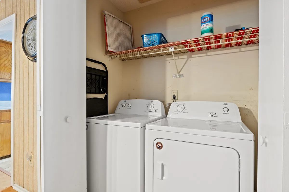 This image captures a practical laundry area, complete with a washing machine, dryer, and a shelf for storage. The scene is tidy and functional, highlighting the convenience of in-unit laundry for guests.