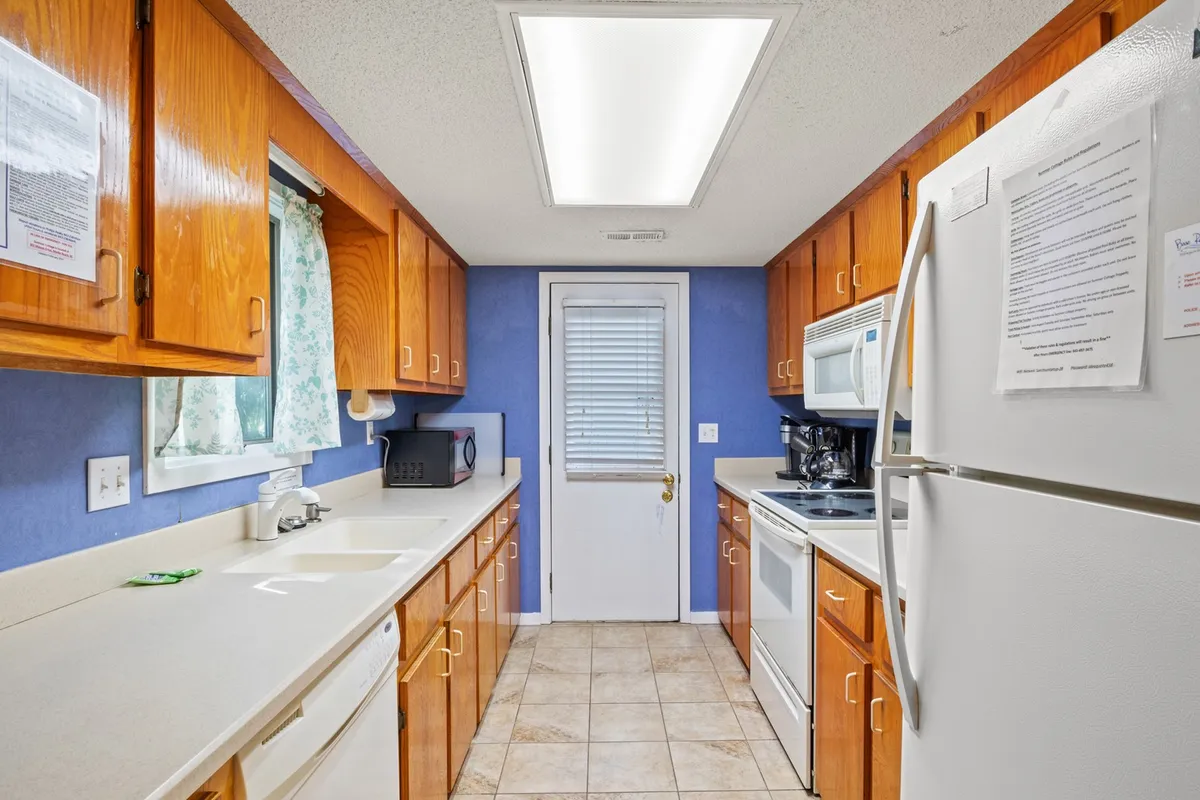 A bright, inviting kitchen with modern countertops, appliances, a window draped with curtains, and a door leading outside. The scene suggests a comfortable space for cooking, gathering, and preparing meals during extended stays.