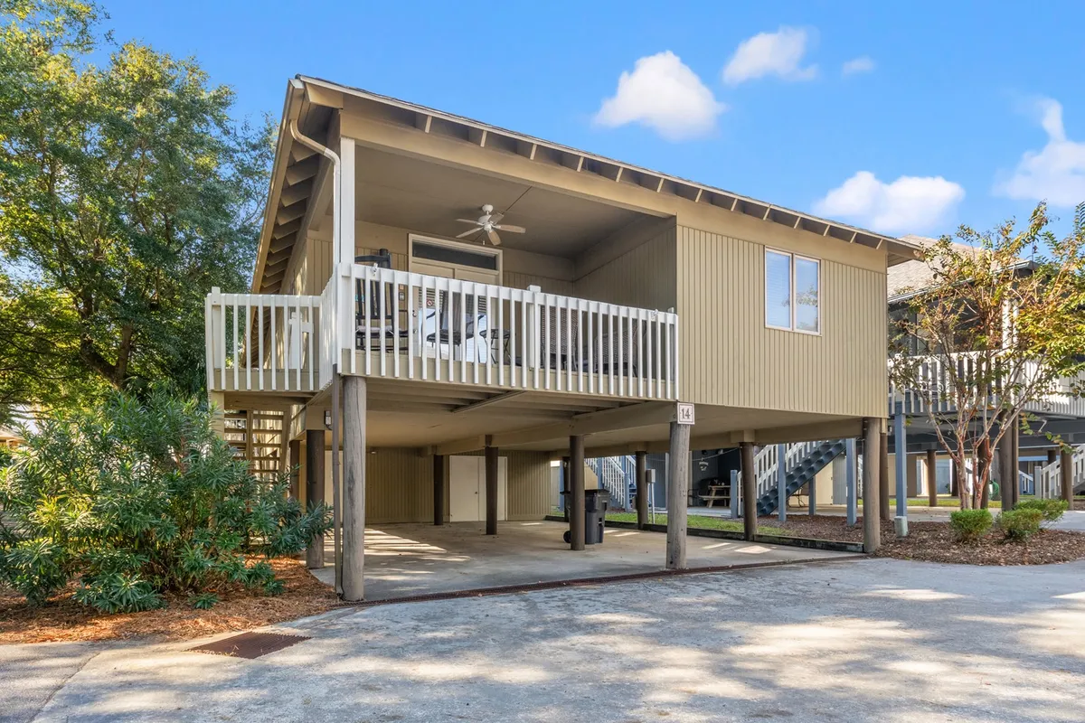The hero image showcases the charming exterior of a free-standing cottage, featuring an elevated porch surrounded by lush greenery and set against a bright, clear sky, evoking a tranquil, inviting atmosphere. The porch is the focal point, suggesting a perfect spot for relaxation, while the surrounding landscaping hints at privacy and serenity. The overall scene radiates calmness and the enjoyment of coastal outdoor living.